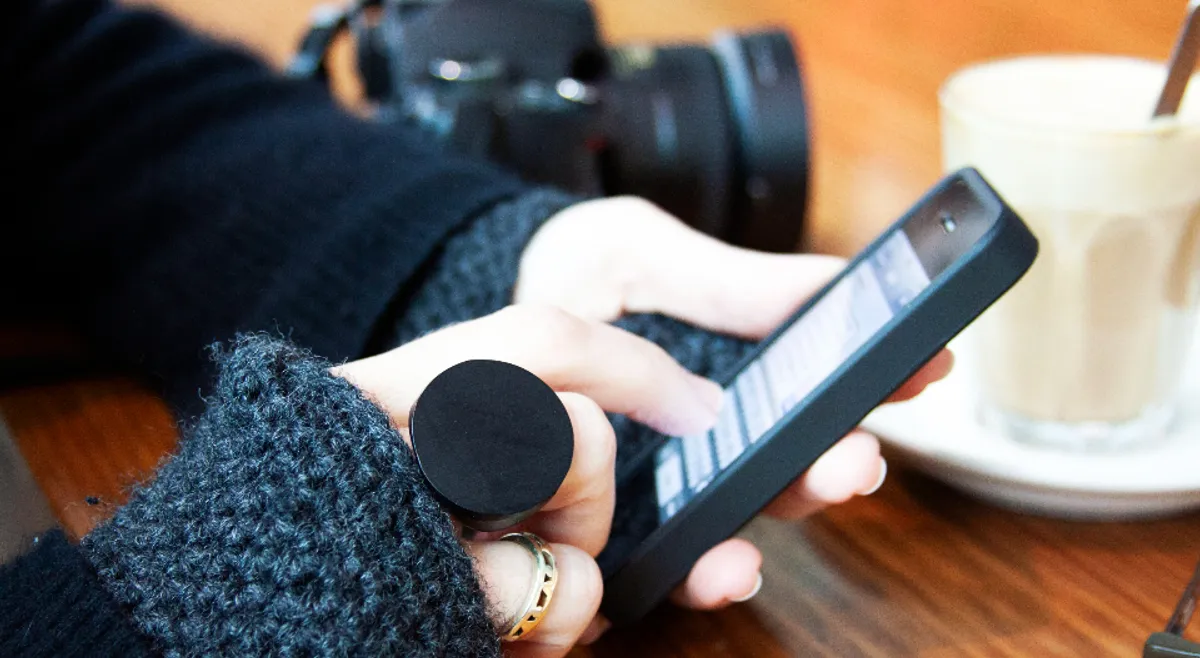 A hand holding a smartphone beside a coffee cup and a camera