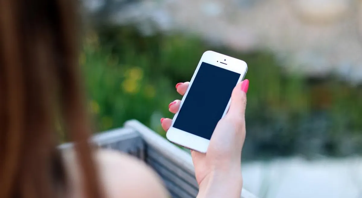 A hand holding a smartphone with a dark screen outdoors