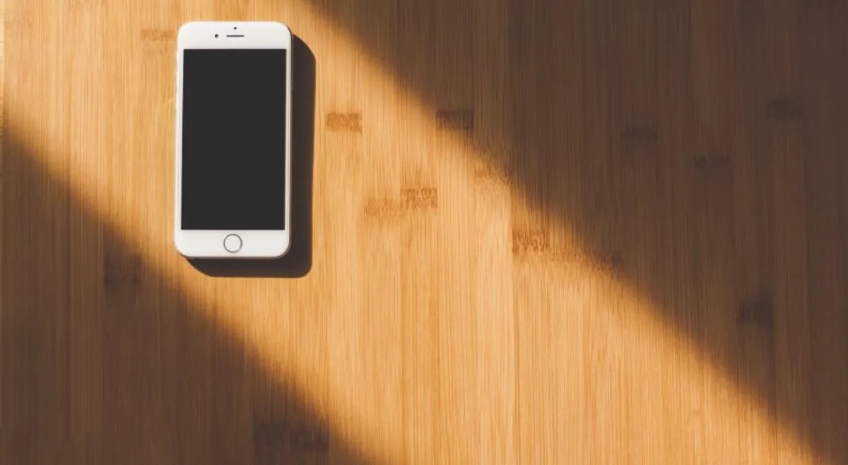 A smartphone lying on a wooden table in a strip of sunlight
